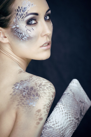 fashion portrait of pretty young woman with creative snake make up, fashion victim with python skin clutch. face like bagの写真素材