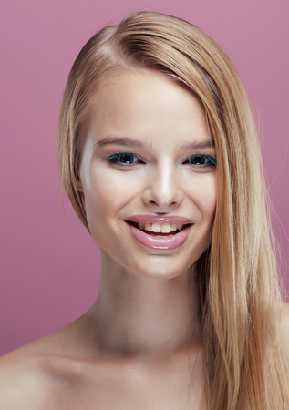 young pretty blonde real woman with hairstyle close up and makeup on pink background smilingの写真素材