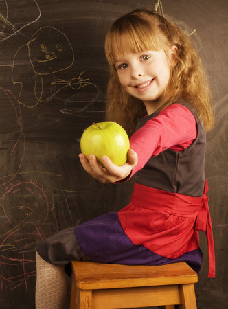 portrait of little cute girl writing on the blackboard with green appleの写真素材