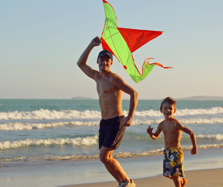 father with son, sunset at the seacoast playing kite, happy family on vacation, silhouetteの写真素材