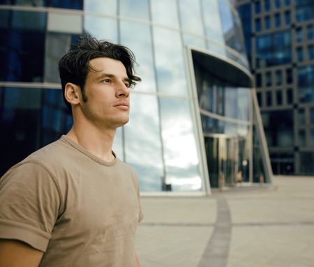 young man stand in front of modern business building, dreams come true, looking somethingの写真素材