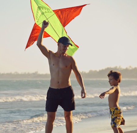 father and son, sunset at the seacoast with kite, happy family on vacation, silhouetteの写真素材