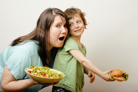 mature fat woman holding salad and little cute boy with hamburger teasing themselvesの写真素材