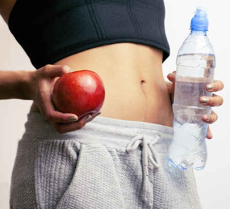 close up woman stomach with hands holding water and reg apple isolatedの写真素材