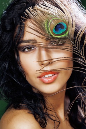 young sensitive brunette woman with peacock feather eyes close up on greenの写真素材