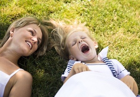 blond mother with daughter having fun on green grassの写真素材