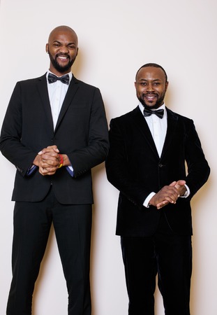 two afro-american businessmen in black suits emotional posing, gesturing, smiling. wearing bow-ties,...