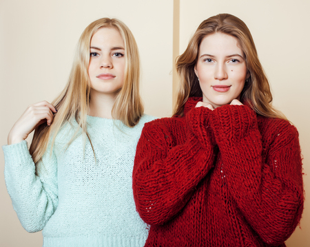 Two young girlfriends in winter sweaters indoors having fun. Lifestyle. Blond teen friends close up smilingの写真素材