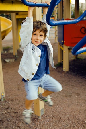 little cute real boy playing on playground, hanging on gymnastic ring cheerful