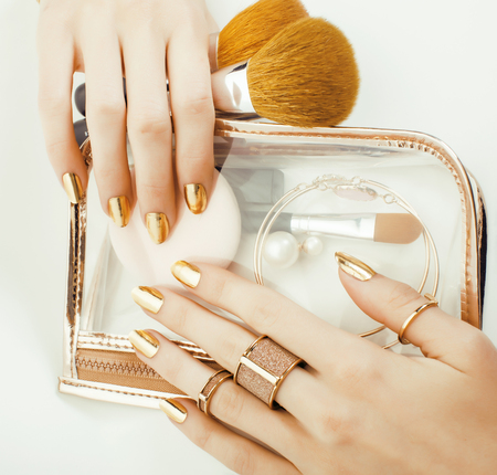 woman hands with golden manicure and many rings holding brushes, makeup artist stuff stylish, pure close up pink flower rose among cosmeticの写真素材