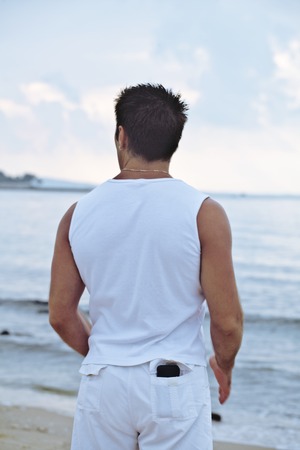 young brunette man on beach at sea smiling, gomosexual in white dress big musclesの写真素材