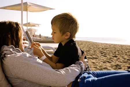 young mother with son resting on sea coast, happy family together talking, lifestyle people conceptの写真素材