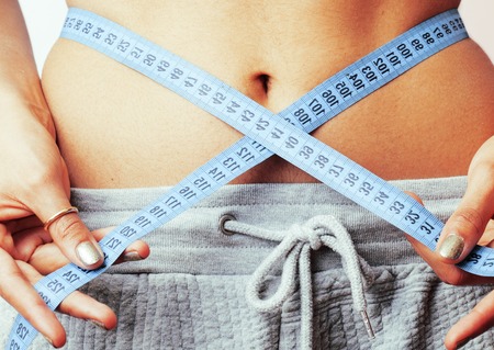 woman measuring waist with tape on knot like a gift, african tann isolated close up white backgroundの写真素材