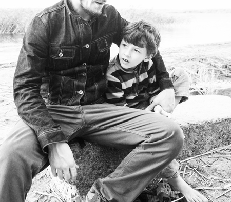 Young father hipster with a beard and his little son on the lake shore. Talking, teaching, having...