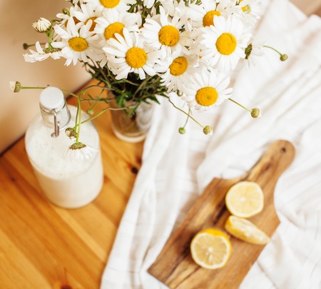 Simply stylish wooden kitchen with bottle of milk and glass on table, summer flowers camomile, healthy food moring concept close upの写真素材