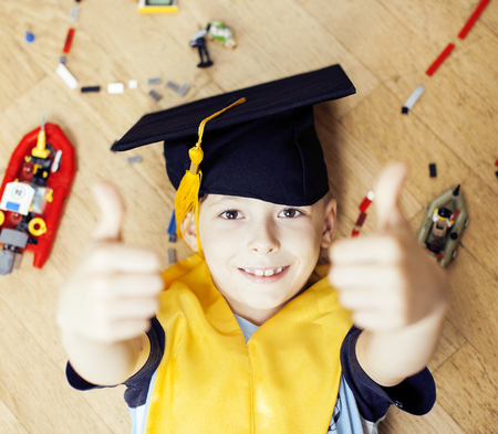 little cute preschooler boy among toys  at home in graduate hat smiling posing emotional, lifestyle people concept, wooden floorの写真素材