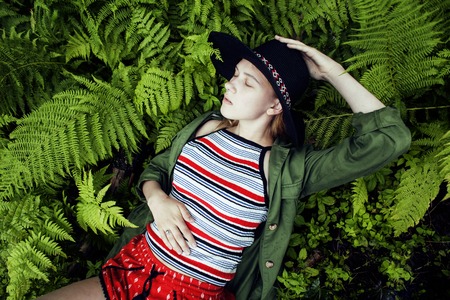 Pretty young blond girl hipster in hat among fern, vacation in green forest, lifestyle fashion people conceptの写真素材