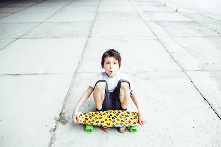 little cute boy with skateboard on playground alone training, making funy faces close upの写真素材