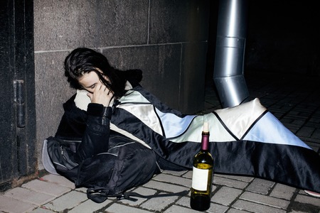 young poor ttenage girl sitting at dirty wall on floor with bottle of vine, poor refugee alcoholic, hopeless homeless woman in depression, real junky concept close upの写真素材