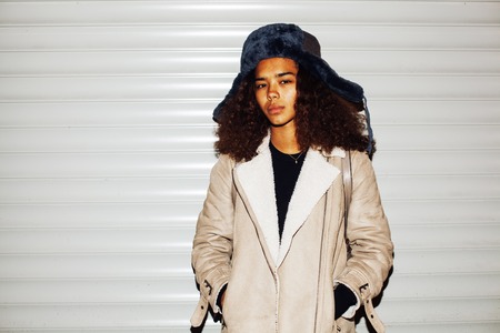 young pretty african american girl teenage outside on street, looking like real junky, social issues concept, red eyes, bum stupid hat, fashion hipster lifestyle people close up mudyの写真素材