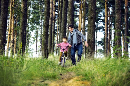 father learning his son to ride on bicycle outside, real happy family in summer forest enjoing nature warm airの写真素材
