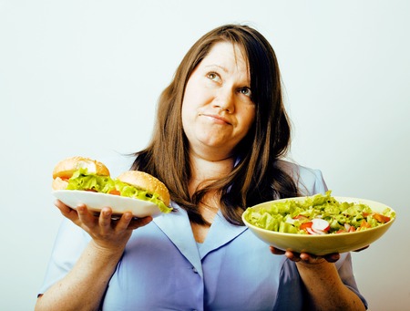 fat white woman having choice between hamburger and salad close up, unhealthy food conceptの写真素材