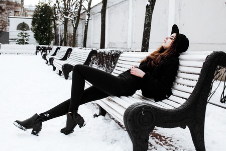 young pretty modern hipster girl waiting on bench at winter snow park alone, lifestyle people concept close upの写真素材