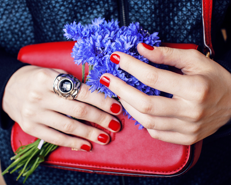 close up portrait of girls manicured hands holding small cute red handbag and cornflower bouquet, lifestyle concept flavorの写真素材