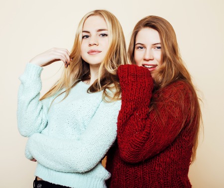 Two young girlfriends in winter sweaters indoors having fun. Lifestyle. Blond teen friends close up smilingの写真素材