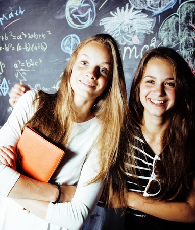 back to school after summer vacations, two teen real girls in classroom with blackboard painted together, lifestyle people conceptの写真素材