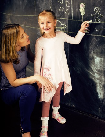 portrait of mature woman teacher with little cute blonde girl pupil writing on blackboard together, lifestyle people conceptの写真素材