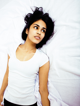 young pretty tan indian mulatto woman in bed among white sheets having fun, trying to sleep, lifestyle people conceptの写真素材