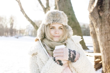 young pretty teenage hipster girl outdoor in winter snow park having fun drinking coffee, warming up...