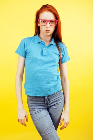 young pretty red hair teenage hipster girl posing in glasses emotional happy smiling on yellow background, lifestyle people conceptの写真素材