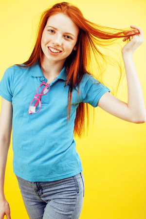 young pretty red hair teenage hipster girl posing in glasses emotional happy smiling on yellow background, lifestyle people conceptの写真素材