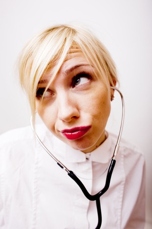young pretty woman doctor with stethoscope emotional posing, pointing in camers, lifestyle people conceptの写真素材