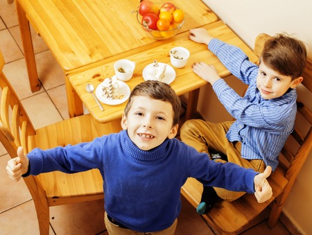 little cute boys eating dessert on wooden kitchen. home interior. smiling adorable friendship together forever friends, lifestyle people conceptの写真素材