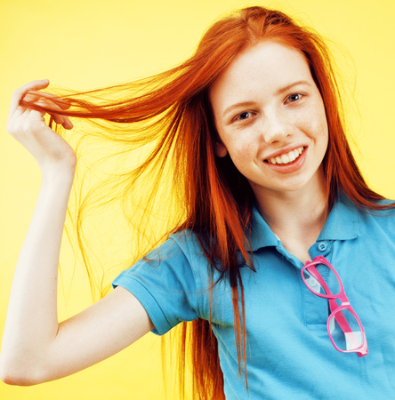 Beauty and skin care. Highly-detailed portrait of attractive redhead teenage girl with charming smile and cute freckles having rest indoors wearing her hair loose. Beautiful woman relaxing at home on yellow backgroundの写真素材