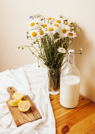 Simply stylish wooden kitchen with bottle of milk and glass on table, summer flowers camomile, healthy food moring conceptの写真素材