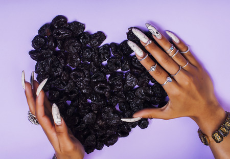 woman hands with long nails manicure holding fruits in shape of heart on purple backgroundの写真素材