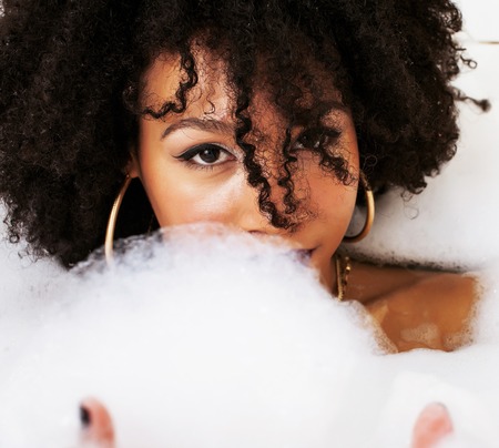 young afro-american teen girl laying in bath with foam, wearingの写真素材