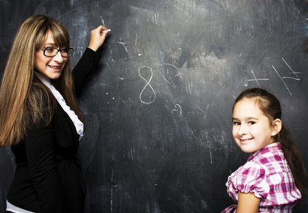 little cute girl with young teacher in classroom studying at bla
