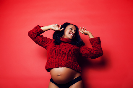 portrait of pregnant woman with big belly, hands hold, red sweatの写真素材