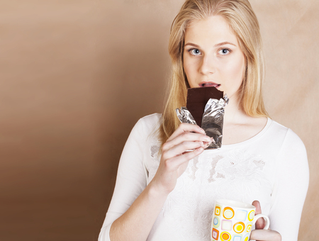young cute blond girl eating chocolate and drinking coffee closeの写真素材