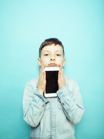 little cute boy posing emotional on blue background with smartphの写真素材