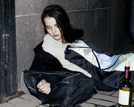 young poor ttenage girl sitting at dirty wall on floor with bottの写真素材