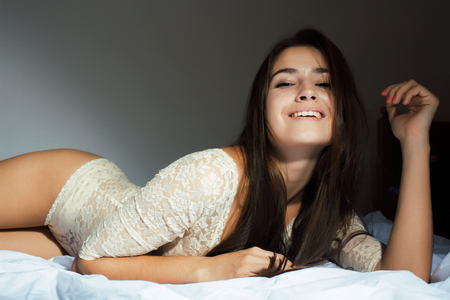 young pretty happy smiling sexy woman in her bed bedroom at nightの写真素材