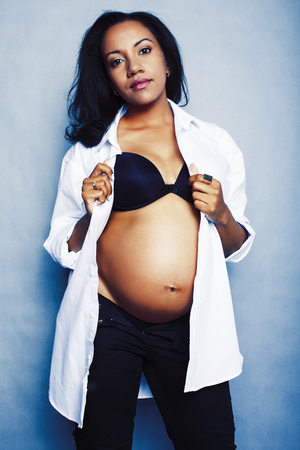 young pretty african american woman pregnant happy smiling, posing stylish on blue background, lifestyle people conceptの写真素材