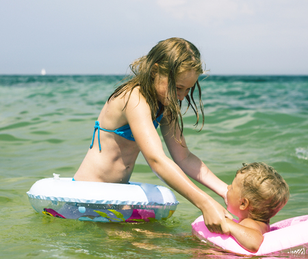 happy children playing in sea, sister helping brother to swim, lifestyle vacation people conceptの写真素材
