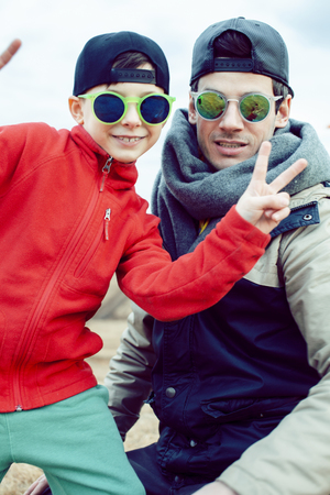 young father with his son having fun outside in spring field, happy family smiling, lifestyle people making selfie wearing sunglassesの写真素材